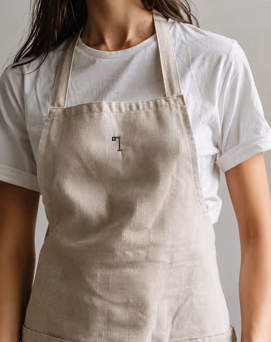 credit chat gpt
woman wearing a beige apron over a white rolled-sleeve t-shirt, with a small brown lamp logomark 
on the apron.