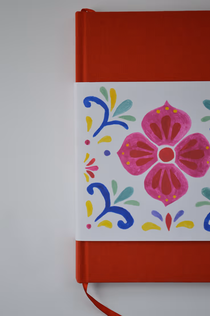 Credit Emilia Piazza. Close up of Dolce y Dulce cookbook with a patterned half-sleeve featuring a pink flower and colorful blue, yellow, and green designs.