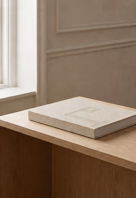 Credit: Chat GPT
Closed beige textured book with embossed logomark design on wooden table near window in neutral room.