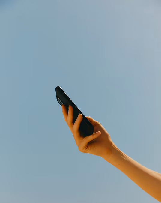 Credit Death to Stock. Hand holding up a black smartphone against a clear blue sky.