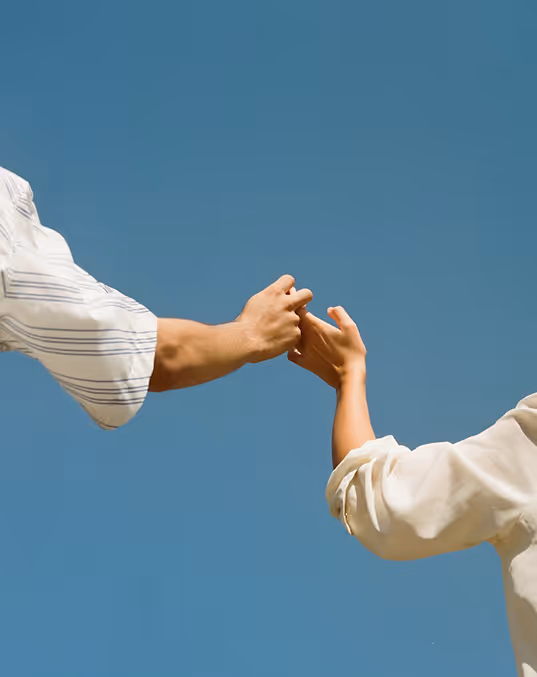Credit: Death to Stock. Two people reaching out and holding hands against a clear blue sky.