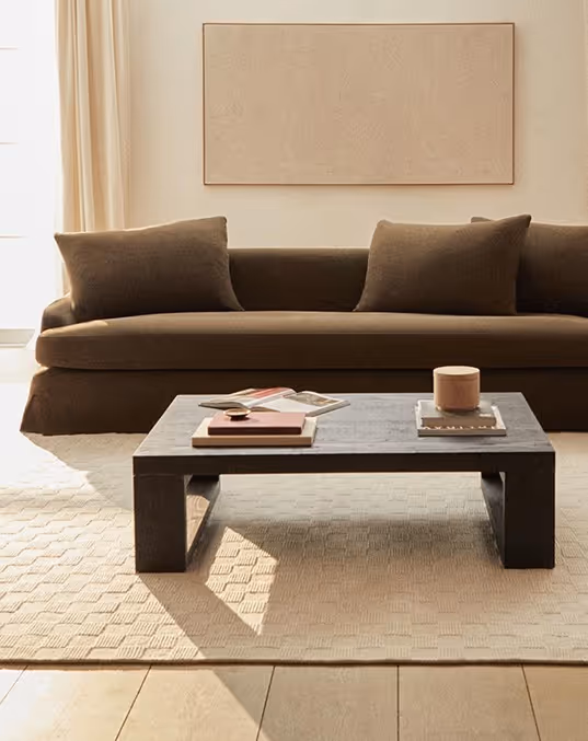 Credit ChatGPT. Brown couch with two pillows behind a dark rectangular coffee table with books and a candle.