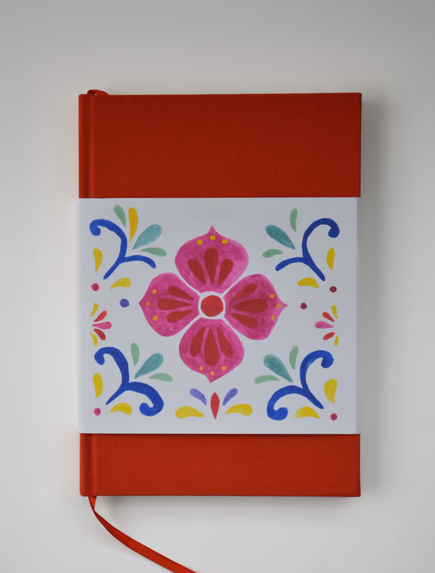 Credit Emilia Piazza. Red hardcover Dolce y Dulce cookbook with a patterned half-sleeve featuring a pink flower and colorful blue, yellow, and green designs.