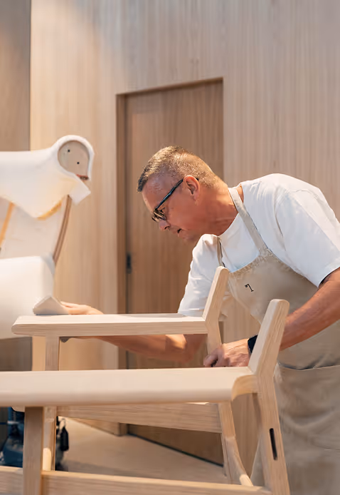 Credit ChatGPT
Man restoring wooden chairs at Les Gaspilleurs workshop wearing beige apron with lamp logo