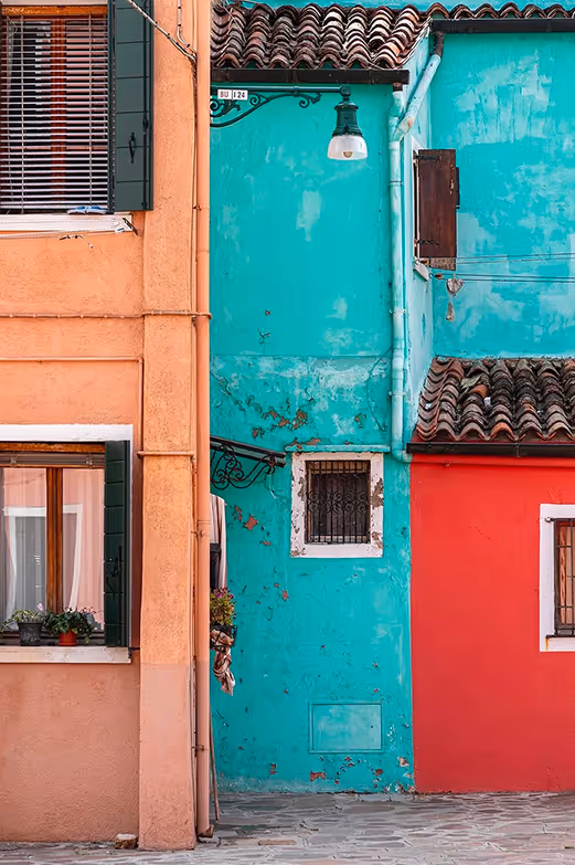 Credit: Jamie Gianfelice. Colorful italian homes with orange, turquoise, and red walls, small windows, and tiled roofs.
