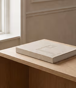 Credit: ChatGPT.  beige book with an embossed lamp detail on a wood table near a window and beige wall.