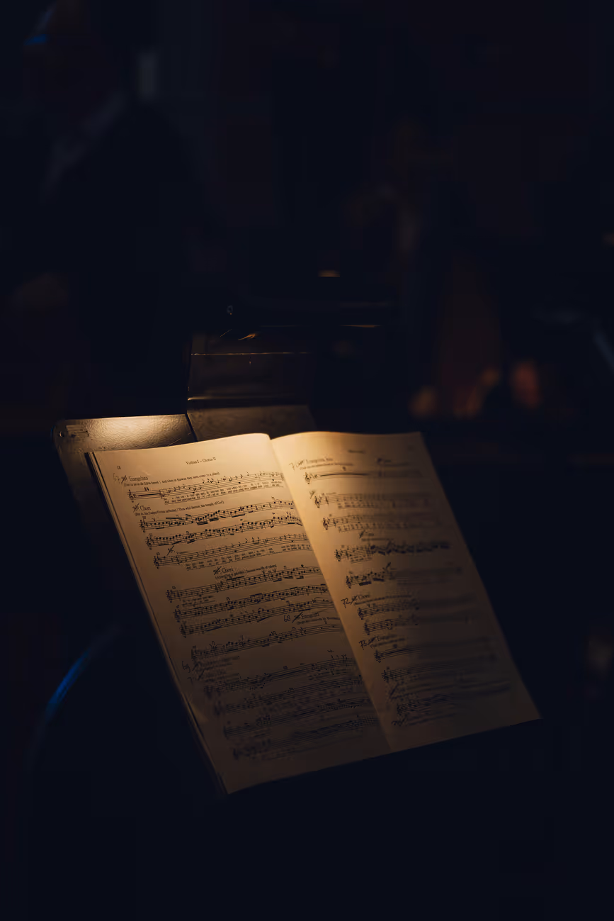 Credit, Unsplash: Marcel Smits
Sheet music illuminated by a warm light on a music stand in a dark room.