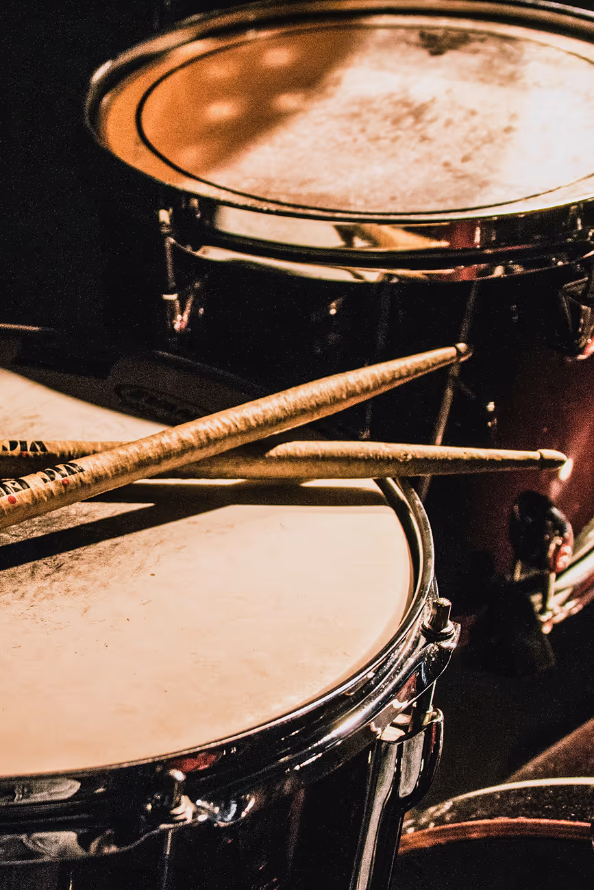 Credit: Unsplash: 
Matthijs Smit
Close-up of drum set with two wooden drumsticks resting on the drumhead in warm light.
