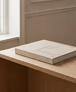 Credit: ChatGPT. beige les gaspilleurs coffee table book on wooden table with light beige wall background.