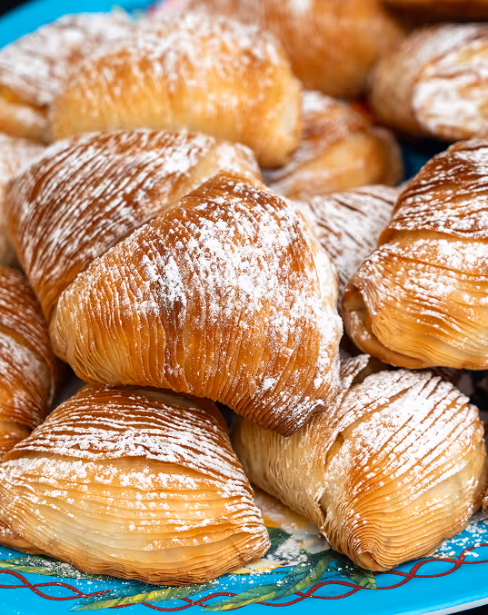 Credit: iStock: Oksana Ermak
Stack of sfogliatella pastries with powdered sugar on a decorative blue ceramic plate.